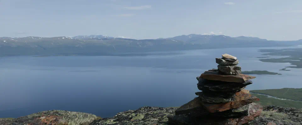 Ett röse av platta stenar på en klippig fjälltopp, med den stora sjön Torneträsk och låga fjäll i bakgrunden
