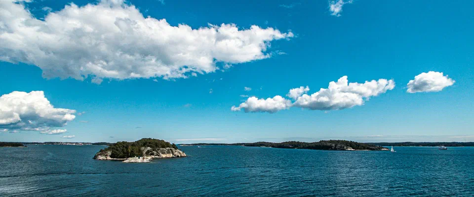 Blått hav med små skogklädda öar och skär under blå himmel med vita moln