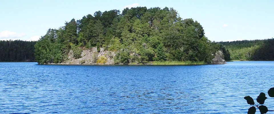 Liten skogsklädd ö mitt i en blank, blå sjö under klar himmel